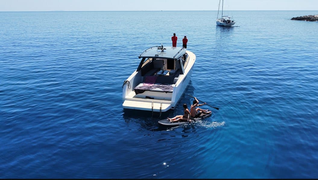 Off the stern of the cabin speedboat — guests paddling on open water, the crew watching from the roof