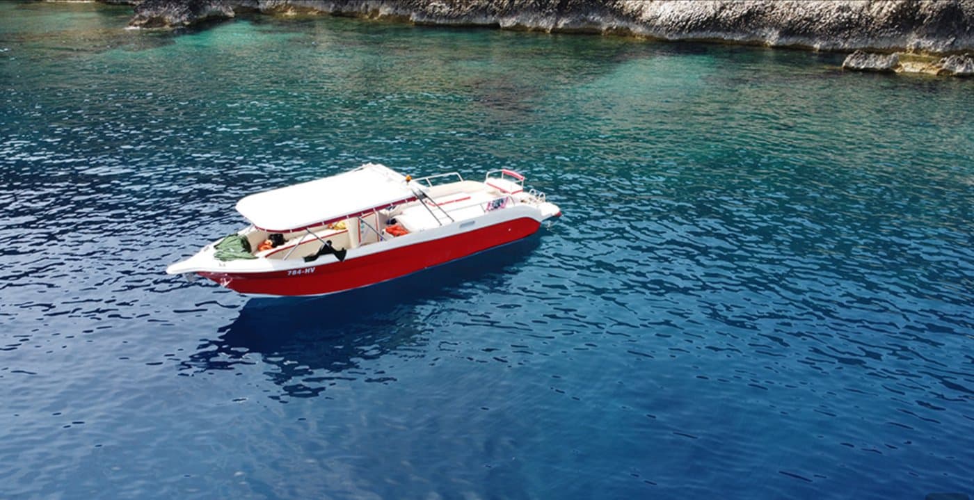 The red Kabina speedboat at anchor in a turquoise Pakleni cove — white canopy over glass-clear water