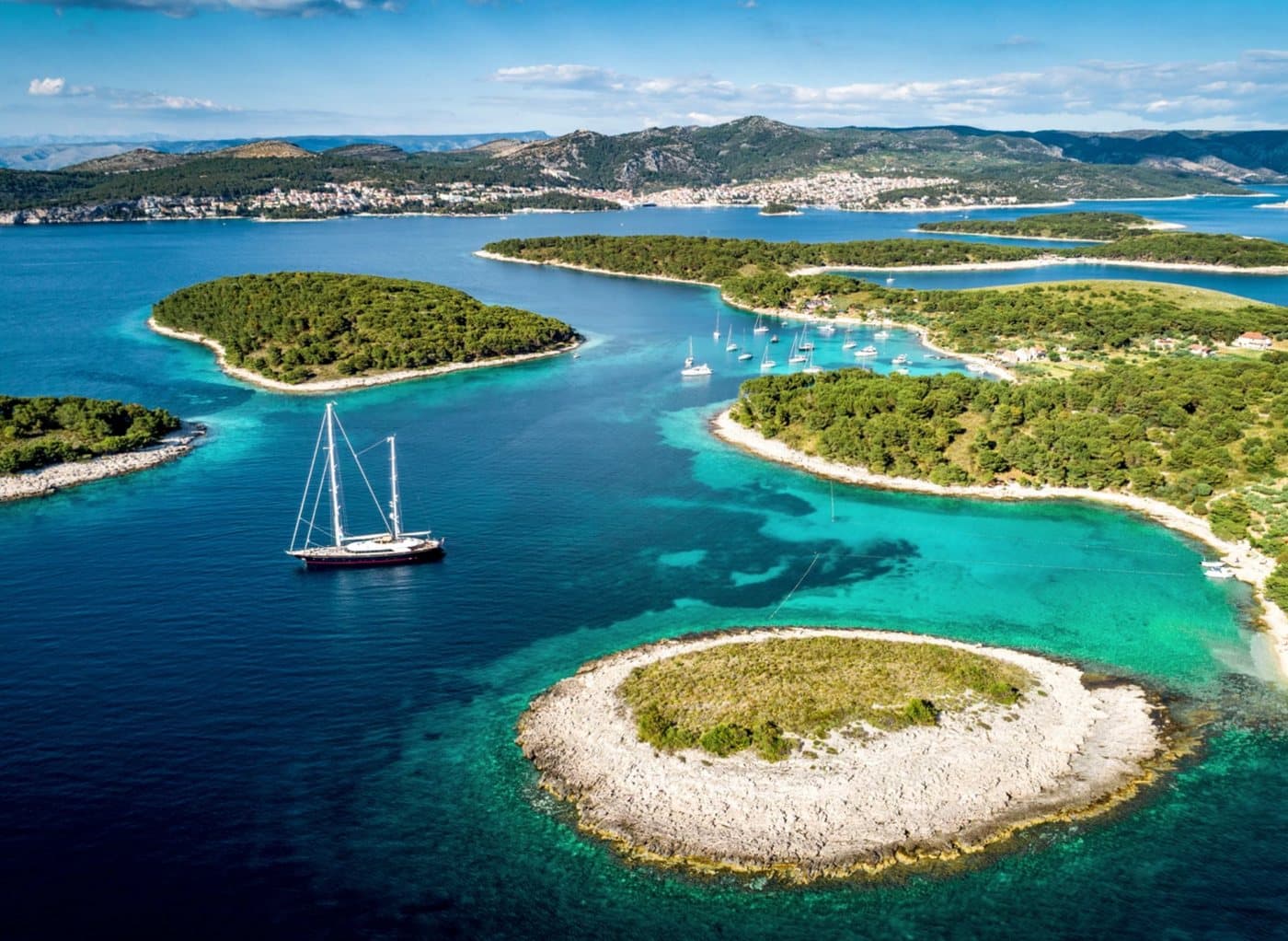 Mlini and the Pakleni islets from the air — turquoise shallows, pine shores and a sailing yacht at anchor