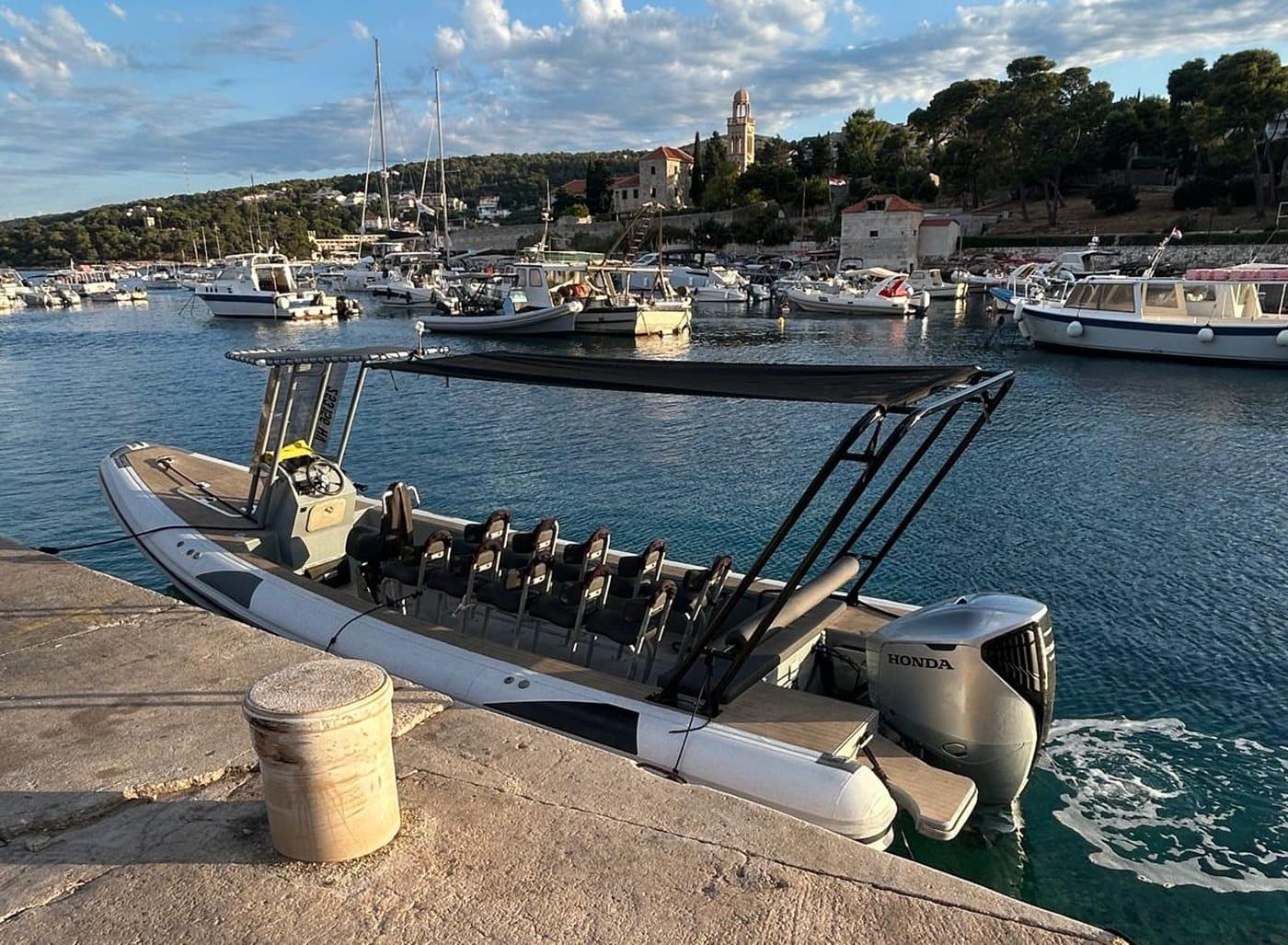 The open Navis Tours boat in Hvar harbour — jockey seats and sun canopy, the campanile behind