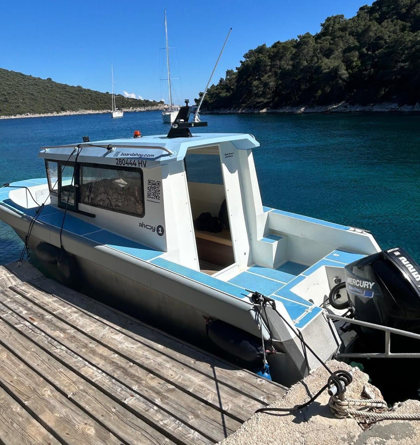 The Navis Tours cabin taxi boat at a Pakleni jetty — turquoise bay and sailboats behind